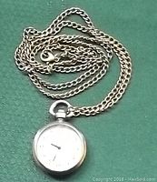 Pendant watch with attached twisted bronze-tone chain necklace laid on green fabric background.