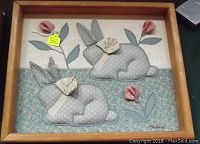 Framed fabric picture with two gray stuffed rabbits, floral background, and pink flowers