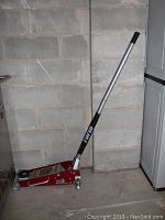 Full view of Torin Big Red hydraulic floor jack, red with a long handle and wheels, standing upright.