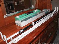 Photo of multiple curtain rods and towel bars on wooden dresser, some rods new in box and others assembled with brackets, colors white, black, and wood finish.