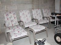 Four metal patio chairs with floral cushions and two matching ottomans positioned in a basement with concrete block walls.