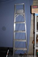 Full view of the 6 foot aluminum ladder standing upright, showing five steps including the top platform, with aluminum construction and a blue backdrop.