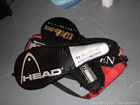 Two racquet bags, one branded Head with black and white colors, the other Wilson with black and red colors, with the Wilson bag partially underneath the Head bag.