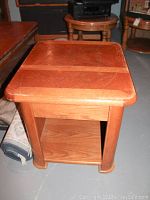 View of rectangular wooden end table with lifted top showing inner area for tray function. Surface shows scratches, dings, and general wear.