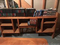 Front view of wooden media storage unit showing multiple compartments, shelves, and built-in CD racks filled with media items.