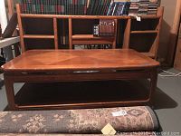 Full frontal view of wooden coffee table showing rectangular shape, diamond pattern top, and open bottom shelf. Background shows bookshelf and chairs.