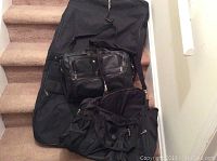 Three black luggage pieces displayed together on carpeted stairs: Pierre Cardin garment bag, Samsonite carryon, and Titleist duffel bag.