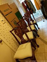 Four wooden dining chairs arranged in a row showing carved backs and upholstered seats