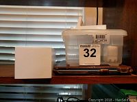 White cube electronics device and plastic container with charger and cables on wooden shelf