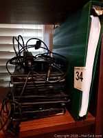 Stack of four black tablets in protective cases with assorted charging cords piled beside a green binder.