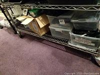 Wide view of metal shelving unit holding multiple plastic bins and boxes labeled 'Old Cell Blkbry Eqpt'.