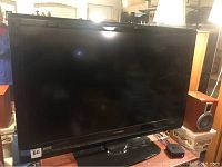 Full view of the NuVision 47-inch LCD monitor on a wooden tabletop with speakers and other objects in the background.