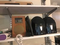 Shelf displaying Tivoli Audio speaker with wooden casing, Sony SRS-X3 speaker, and Mirage limited edition speakers in black.