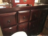 Front view of wider wooden dresser with multiple drawers and metal ring pulls, showing some wear and a damaged spot on the drawer face