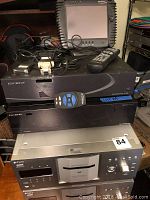 Top view showing two Escient media servers stacked, touchscreen controller on top, remotes and two SX-100 adapters.