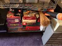 Shelf with multiple board games stacked: Scrabble, Balderdash, Tribond, Scattergories, Phrases educational game.