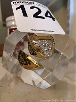 Close-up photo of a gold-tone ring shaped as a bull's head, featuring rhinestones and a MaxSold lot number tag attached.