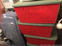 Four plastic storage totes stacked, two red with green lids labeled "Christmas Miscellaneous Fragile" handwritten on the side.