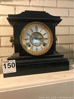 Front view showing the black mantle clock with gold-tone bezel and Roman numeral dial.