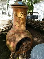Close-up of terracotta chiminea with grapevine design and open fire chamber containing leaves.