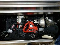 Overview photo inside a drawer showing the cordless drill marked Craftsman, a Black & Decker orange power tool (router), and two reflective shop lights among various cords.