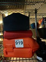 Orange Black and Decker drill bit set case stacked with another black case on metal shelf.