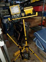 Wide view of two yellow adjustable work lights mounted on tripods with power cords in storage area.