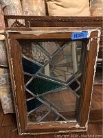 Leaded glass window in brown wood frame with geometric radiating pattern, blue label “14×21”