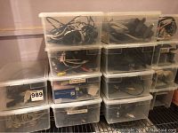 Overall view of multiple stacked plastic containers filled with various computer cables and power cords.