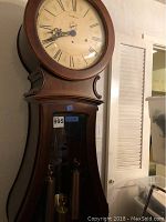 Full view of wooden pendulum clock leaning against wall