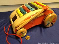 Wooden toddler pull toy with colorfully painted metal xylophone keys and orange pull string next to a coin for scale.