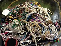 Photo showing a pile of various costume jewelry including beaded necklaces, bracelets, and earrings of mixed colors and materials.