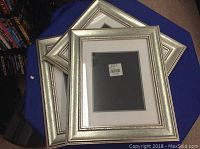 Three matching silver decorative picture frames on a blue cloth surface
