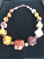 Top view showing a necklace with cubes and cuboctahedron-shaped Moakite Jasper beads in multiple earthy colors on a black background.