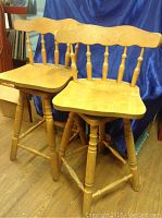 Pair of hardwood swivel stools showing full view of both stools side by side on wood floor with blue draped backdrop.