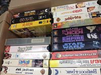 Photo showing VHS movies including Star Wars trilogy, Ace Ventura, Show Boat, and several others stacked in a box.