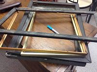 Five old wooden picture frames stacked and laid out on a wood surface with a blue marker for scale.