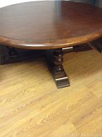 Photo of the round wooden coffee table surface and one of its turned pedestal legs and base to show condition and detailing.