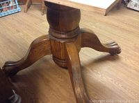 Close-up of the oak table pedestal base showing the center column and four outward curved legs ending in rounded feet.
