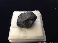 View of smooth, polished black Apache Tear obsidian stone placed on a white cushioned padded base.