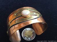 Copper and brass cuff bracelet with central round opal gemstone, showing hammered copper texture and brass accents.