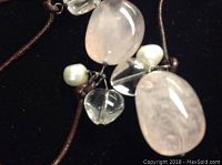 Close-up of polished rose quartz stones, clear quartz beads, baroque pearls attached to the brown leather cord.