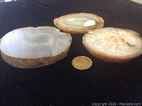 Three agate slices shown on dark cloth with a coin for size comparison, displaying their varying sizes and matte finishes.