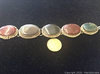 Front view of bracelet displaying five polished oval jasper stones with a coin for size comparison showing the bracelet length.