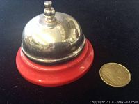 Side angle view of the vintage bell showing the polished silver-tone dome and red base, with a coin for size reference.