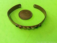 Copper open cuff bracelet with 7 round chakra stones embedded along the top and two magnets on the inner side, shown alongside a coin for size reference.