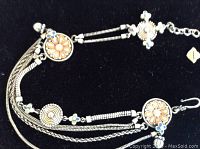 Top down view of silver floral design anklet with orange and blue enamel accents displayed on black background.
