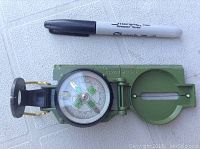 Photo of top side of green Sheffield directional compass with open sighting mirror and visible compass dial, next to a black Sharpie marker for size reference.
