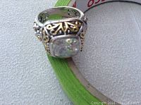 Front angled view showing ornate band and large rectangular clear faceted stone