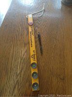 Photo of the front side of the yellow hockey stick backscratcher showing the handwritten text and four beer caps attached.